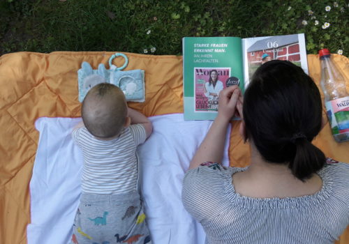 Mutter und Sohn liegen auf dem Bauch auf einer Decke im Park und lesen