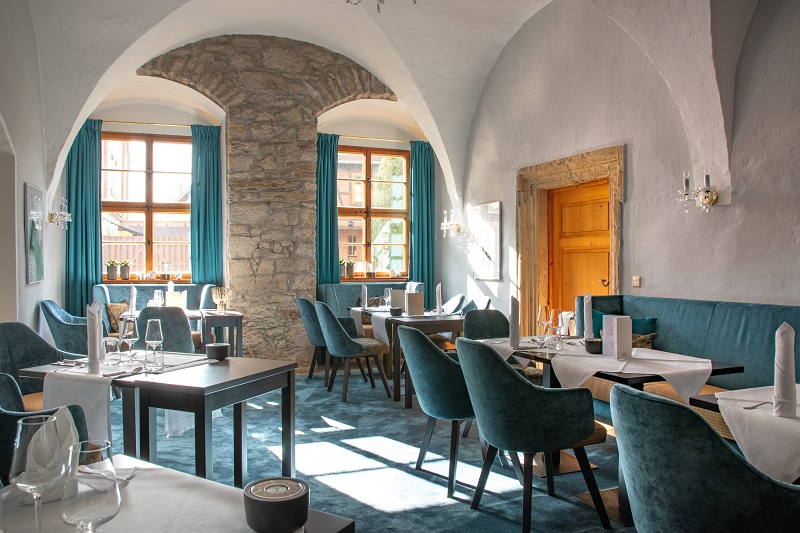 Blick in ein Zimmer mit Gewölbedecke im Restaurant "Reinhardt's im Schloss". Möbel und Vorhänge sind in sanften Blautönen gehalten.