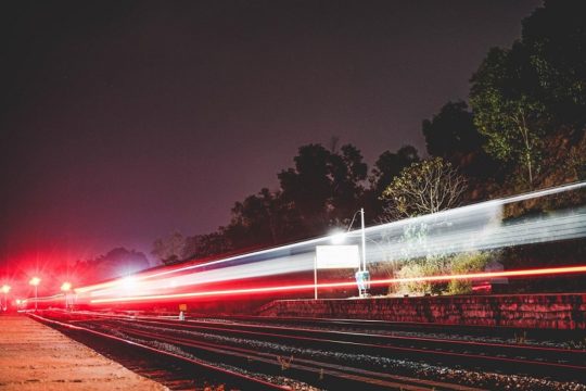 Ein Zug fährt in der Nacht am Bahnhof entlang - man sieht in der Langzeitaufnahme nur die Zuglichter