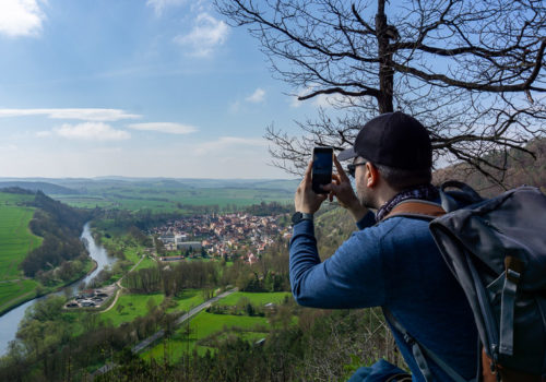 Ein junger Mann fotografiert die Aussicht auf einem Aussichtspunkt auf den Ebenauer Köpfen. In der Ferne sieht man links die Werra und rechts daneben die Stadt Creuzburg.