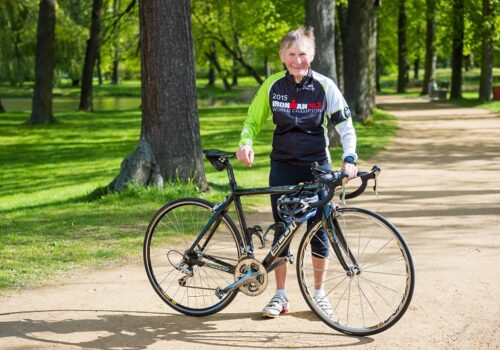 Elisabeth Onißeit steht in ihrem Ironman Hawaii Trikot hinter ihrem Rennrad auf einem Weg im Park.