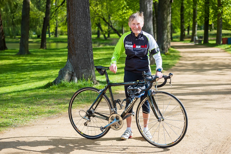 Elisabeth Onißeit steht in ihrem Ironman Hawaii Trikot hinter ihrem Rennrad auf einem Weg im Park.